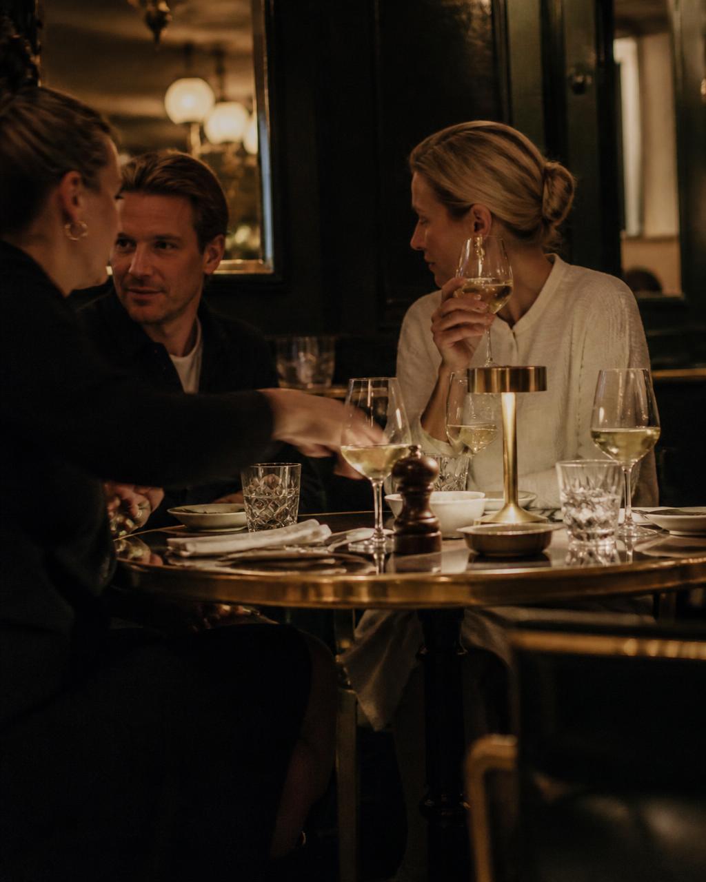 Kollegor i kvällsljus runt ett bistrobord med vinglas efter arbetsdagen